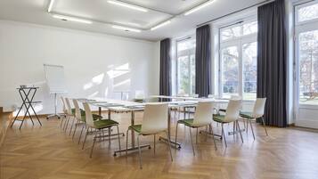 Une salle de conférence équipée d’une grande table, de chaises, d’un tableau blanc et de grandes fenêtres avec des rideaux.