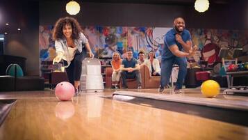 A bowling alley with a wooden floor, a pink bowling ball, and a yellow bowling ball.