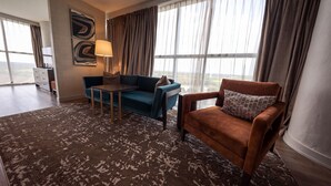 A modern hotel room with a large window, a blue sofa, a brown armchair, a small table, and a lamp. - Wind Creek Casino & Hotel Atmore (Atmore)