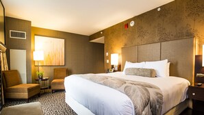 A hotel room with a large bed, two chairs, a desk, and a wall-mounted TV.