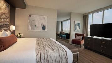 Una habitación de hotel con una cama grande, un televisor de pantalla plana, una zona de estar con sofá y sillones, y obras de arte en las paredes.