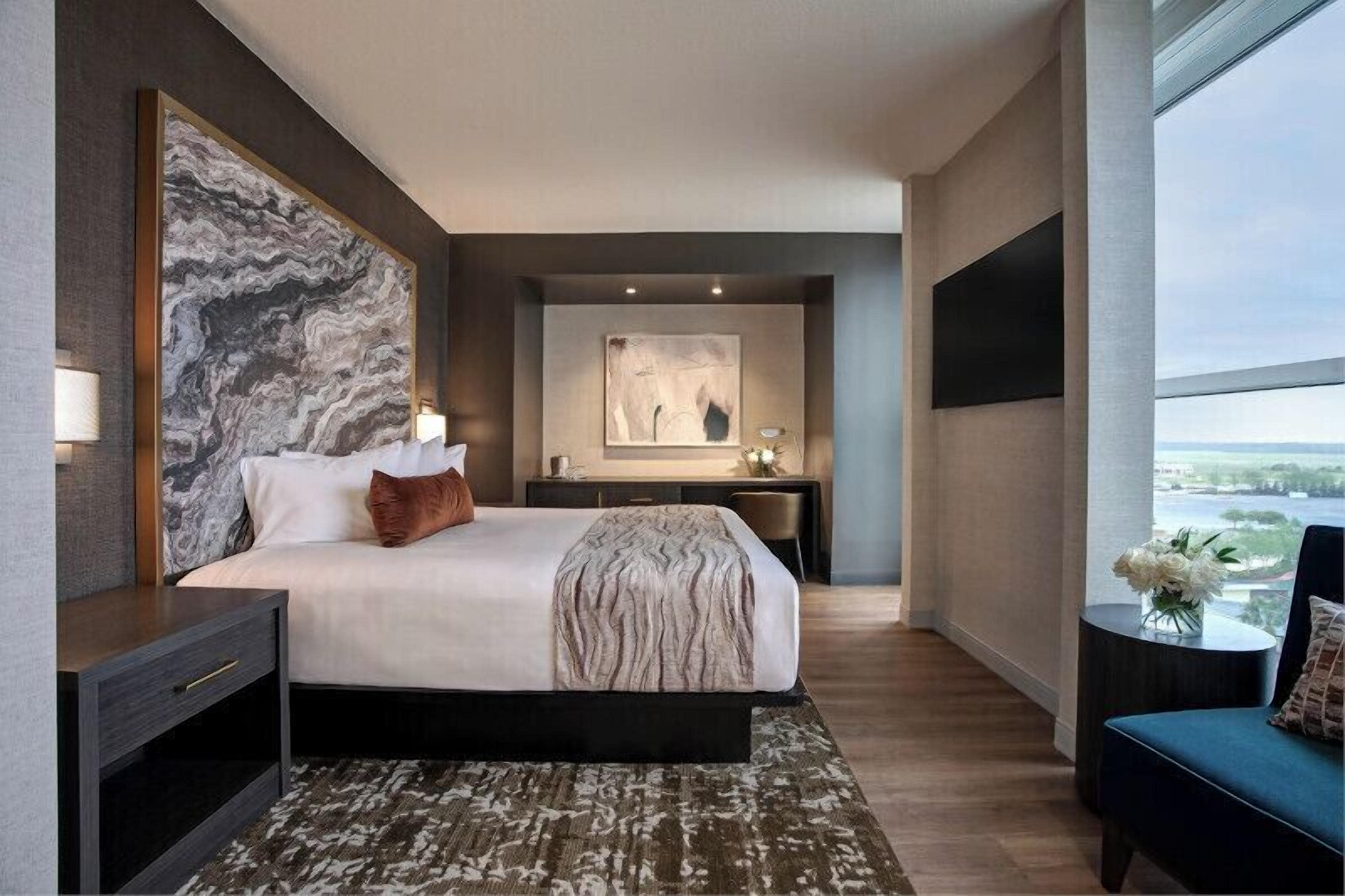 A modern hotel room with a large bed, a desk, and a view of the city.