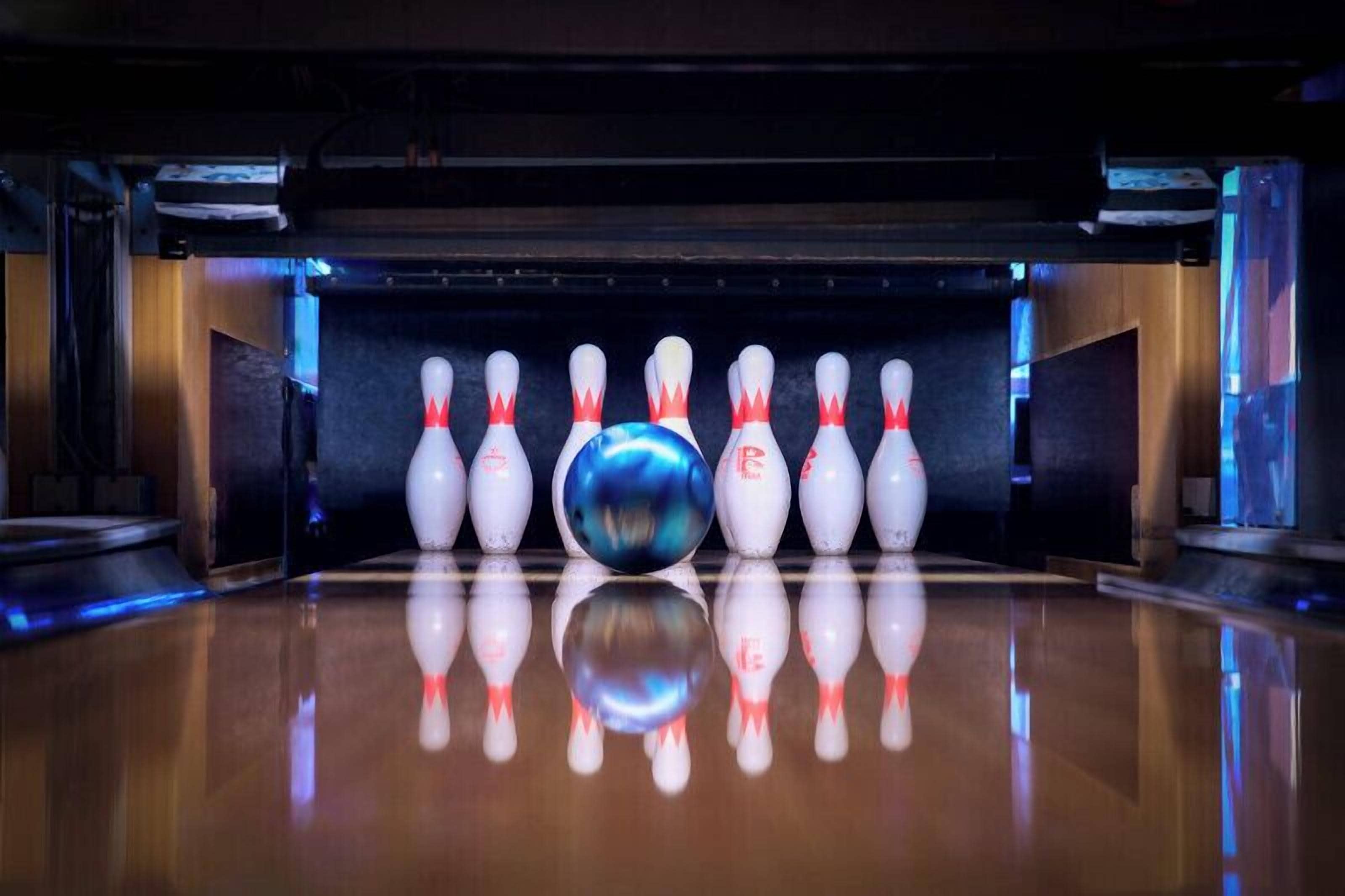 A bowling alley with a polished wooden floor and a row of white bowling pins with red tops.