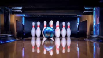 Een bowlingbaan met een glanzende houten vloer en een rij witte bowlingpinnen met rode dopjes.