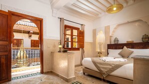 A bedroom with a bed, bedside table, lamp, and a view through an open door to a balcony. - Riad Atlas Acacia (Marrakech)