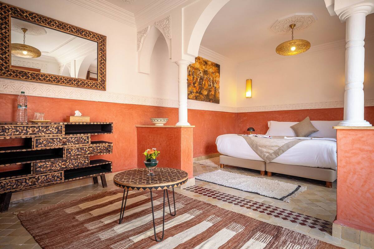 A bedroom with a bed, a bedside table, a mirror, a wall art piece, and a decorative column.