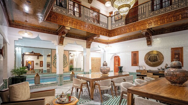 A spacious interior with a high ceiling, ornate wooden balcony, and a central dining area with chairs and a table. - Riad Atlas Acacia (Marrakech)
