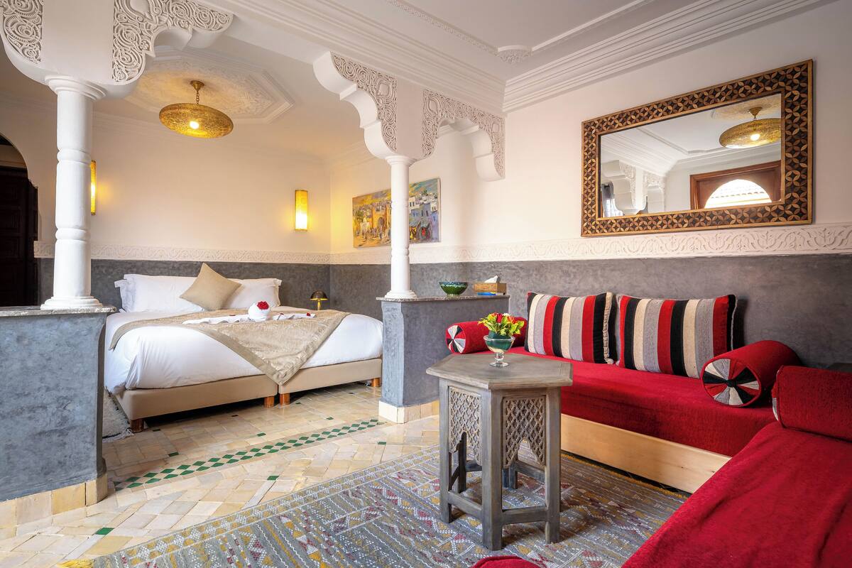 A bedroom with a bed, a red sofa, a small table, and a decorative mirror.