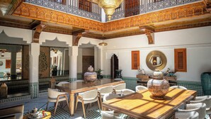 A spacious courtyard with a wooden table, chairs, and ornate ceiling details. - Riad Atlas Acacia (Marrakech)