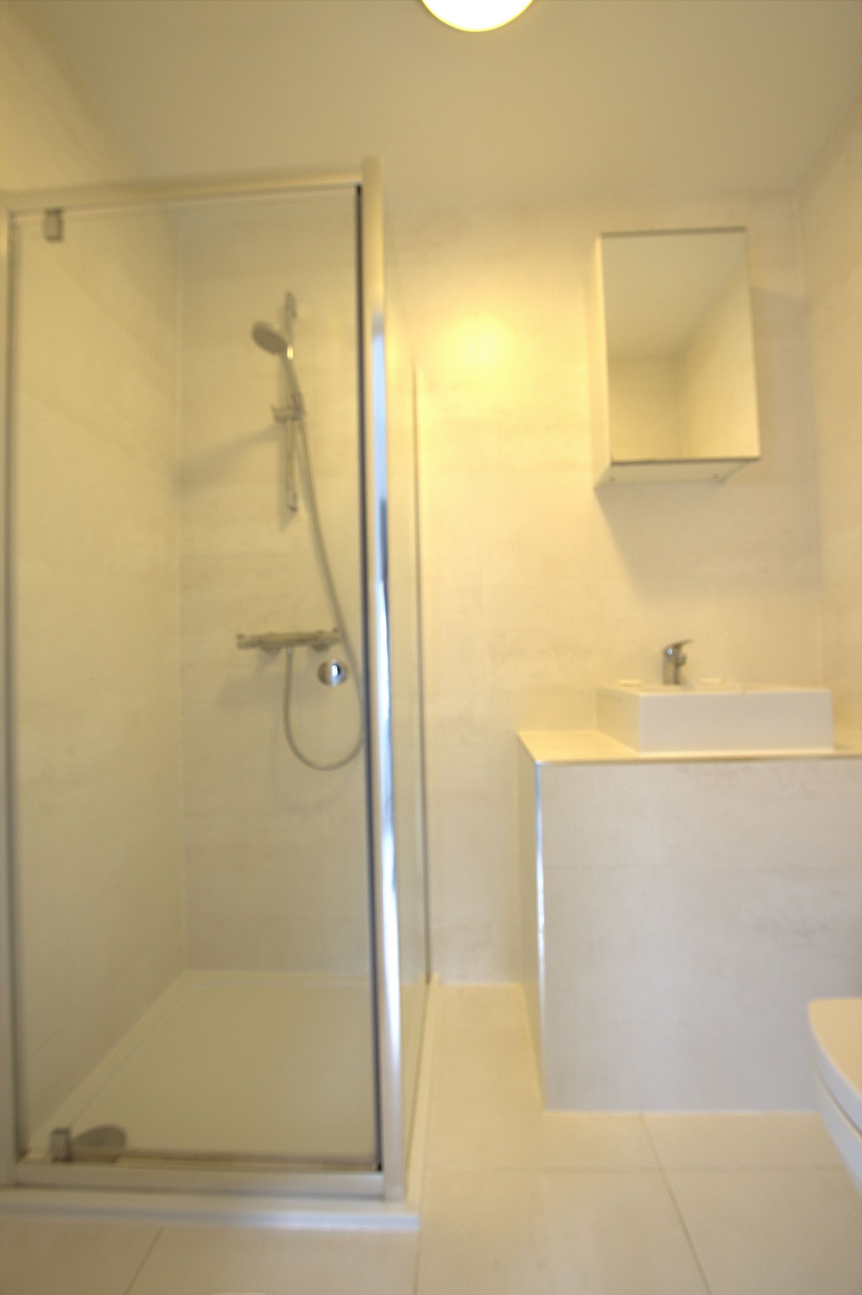 A bathroom with a glass-enclosed shower, a white sink, and a mirror on the wall.