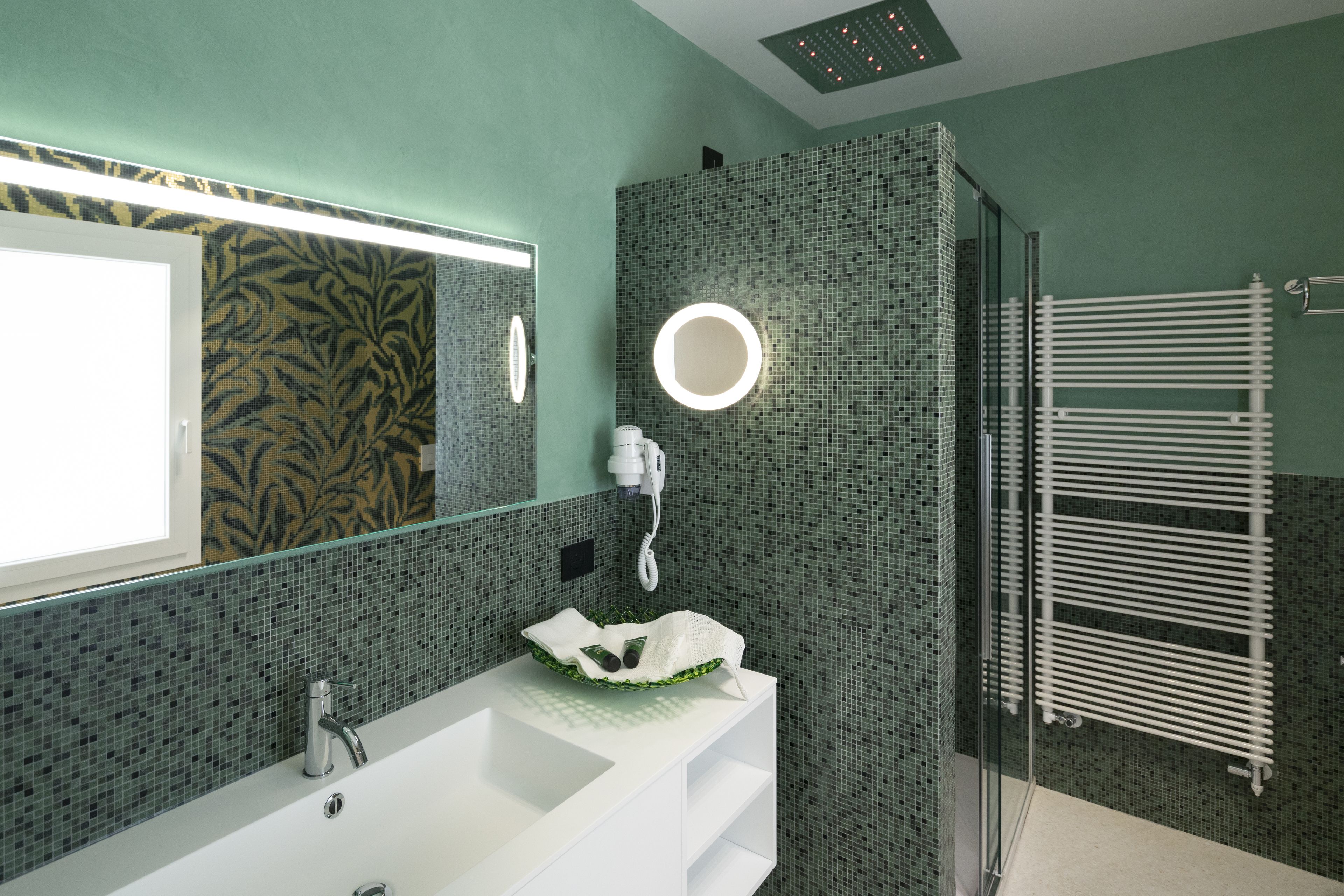 Un baño moderno con un lavamanos blanco, ducha con cerramiento de vidrio y pared de azulejos verdes.