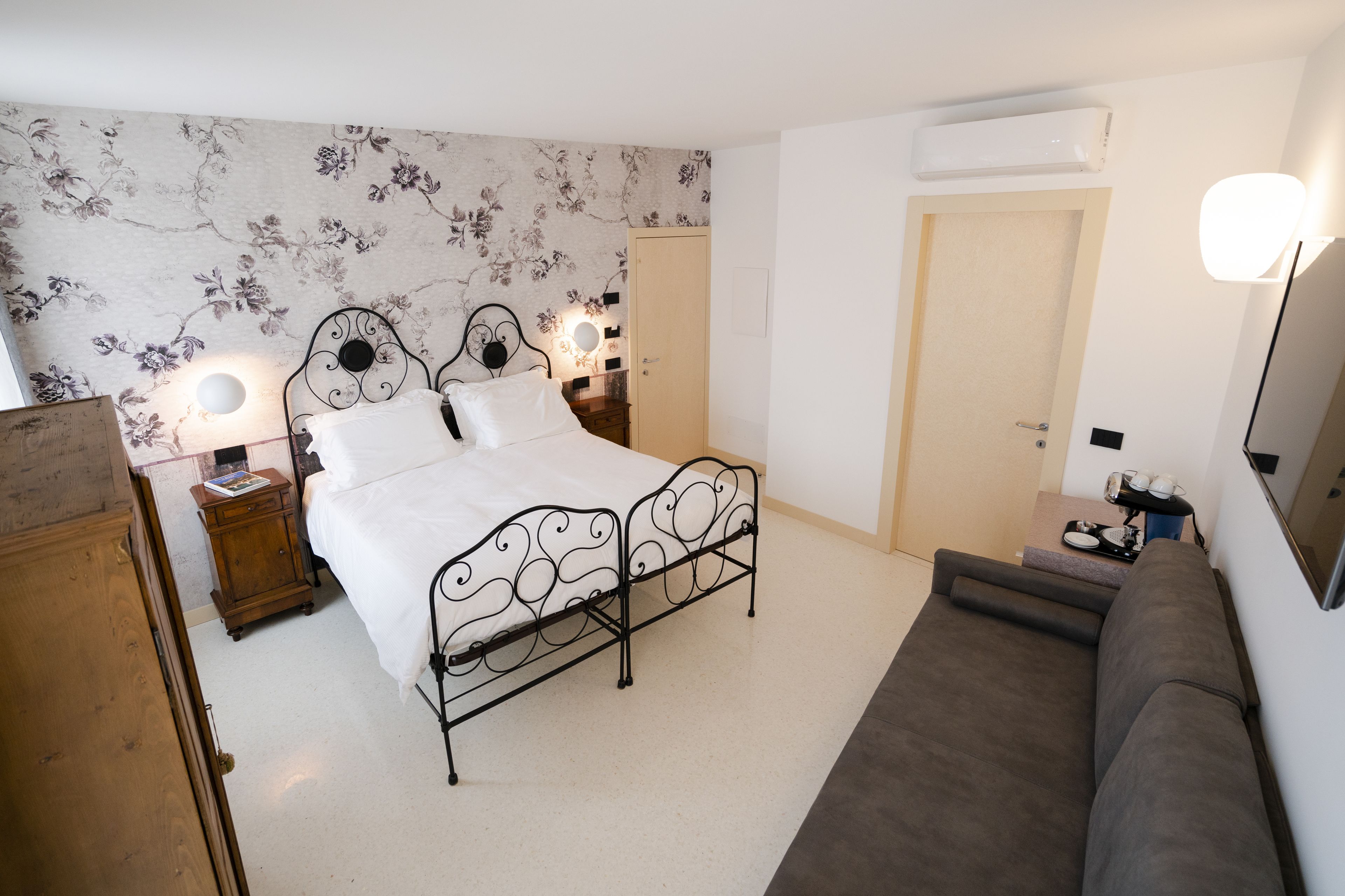 Een slaapkamer met een tweepersoonsbed, een houten nachtkastje, een dressoir, een sofa en een deur.