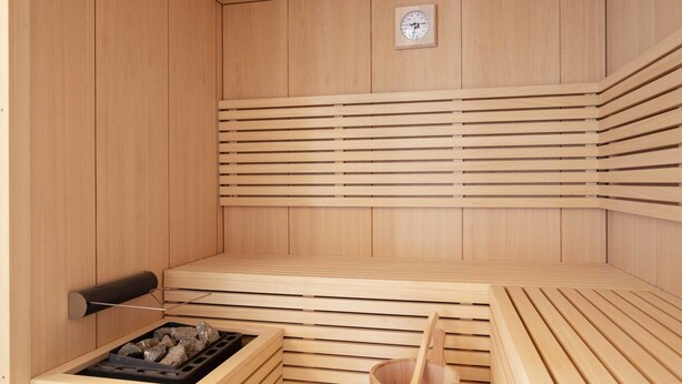 Una sauna de madera con bancos, un calentador para bancos y un balde.