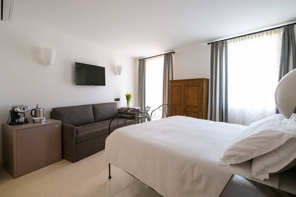 A hotel room with a bed, a sofa, a TV, a wooden wardrobe, and a small table with a plant.