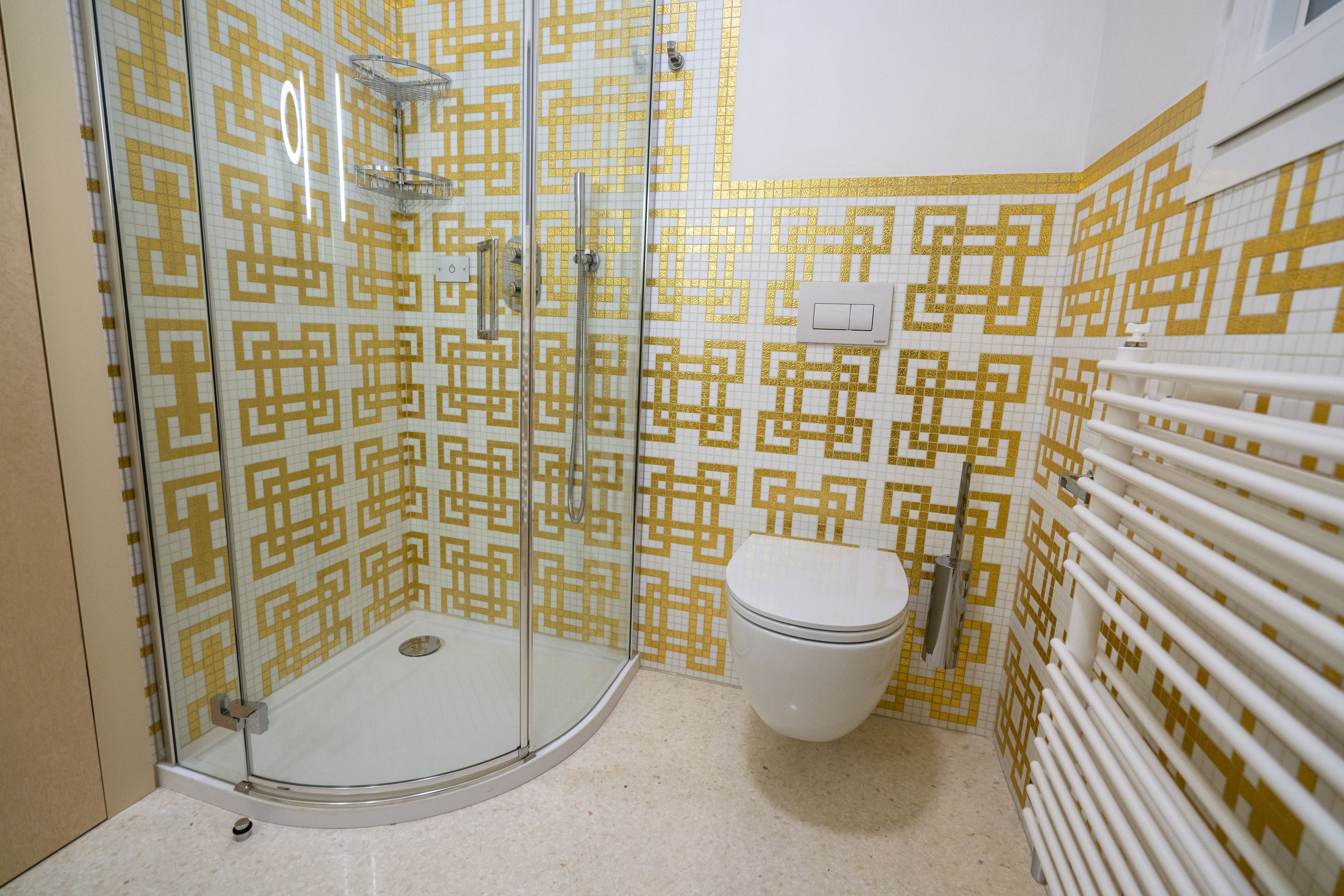 Un baño con ducha de mampara de vidrio, inodoro y pared de azulejos estampados.