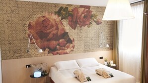 Habitación de hotel con un gran mural floral en la pared, una cama con ropa blanca, una mesita de noche con lámpara y un candelabro colgante.