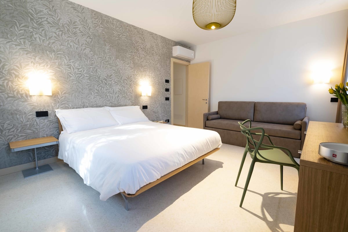 A modern bedroom with a bed, a green chair, a wooden desk, and a sofa.