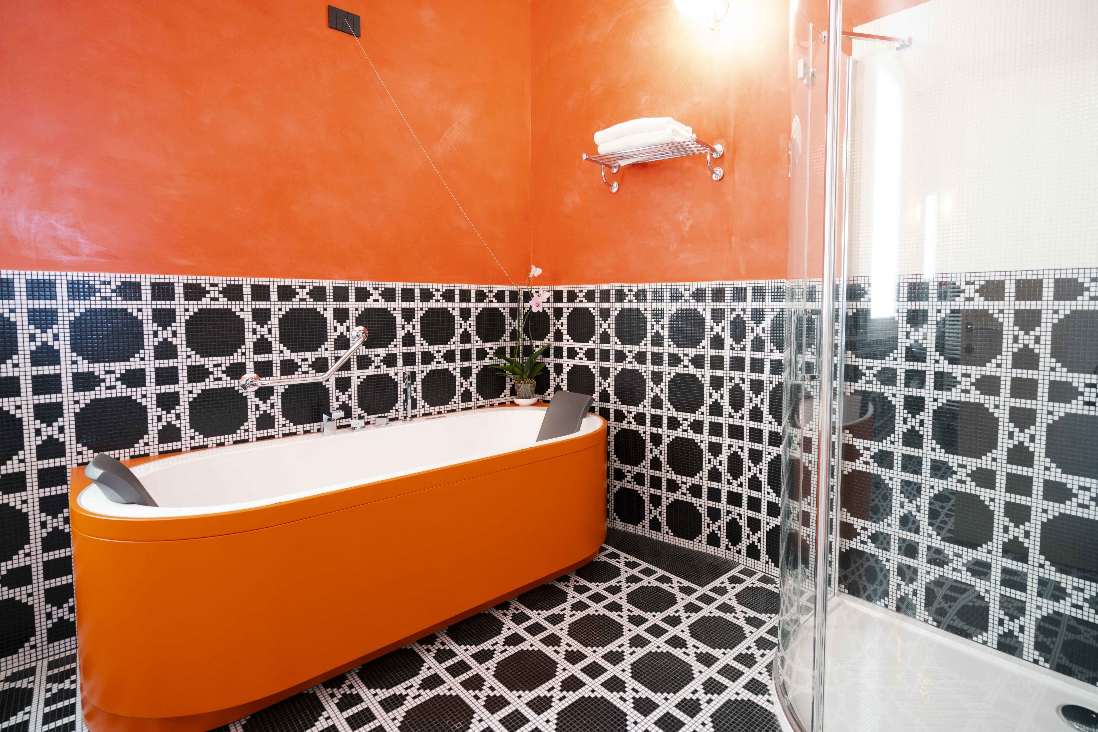Un baño con una bañera moderna color naranja, baldosas estampadas en blanco y negro, y una cabina de ducha de vidrio.