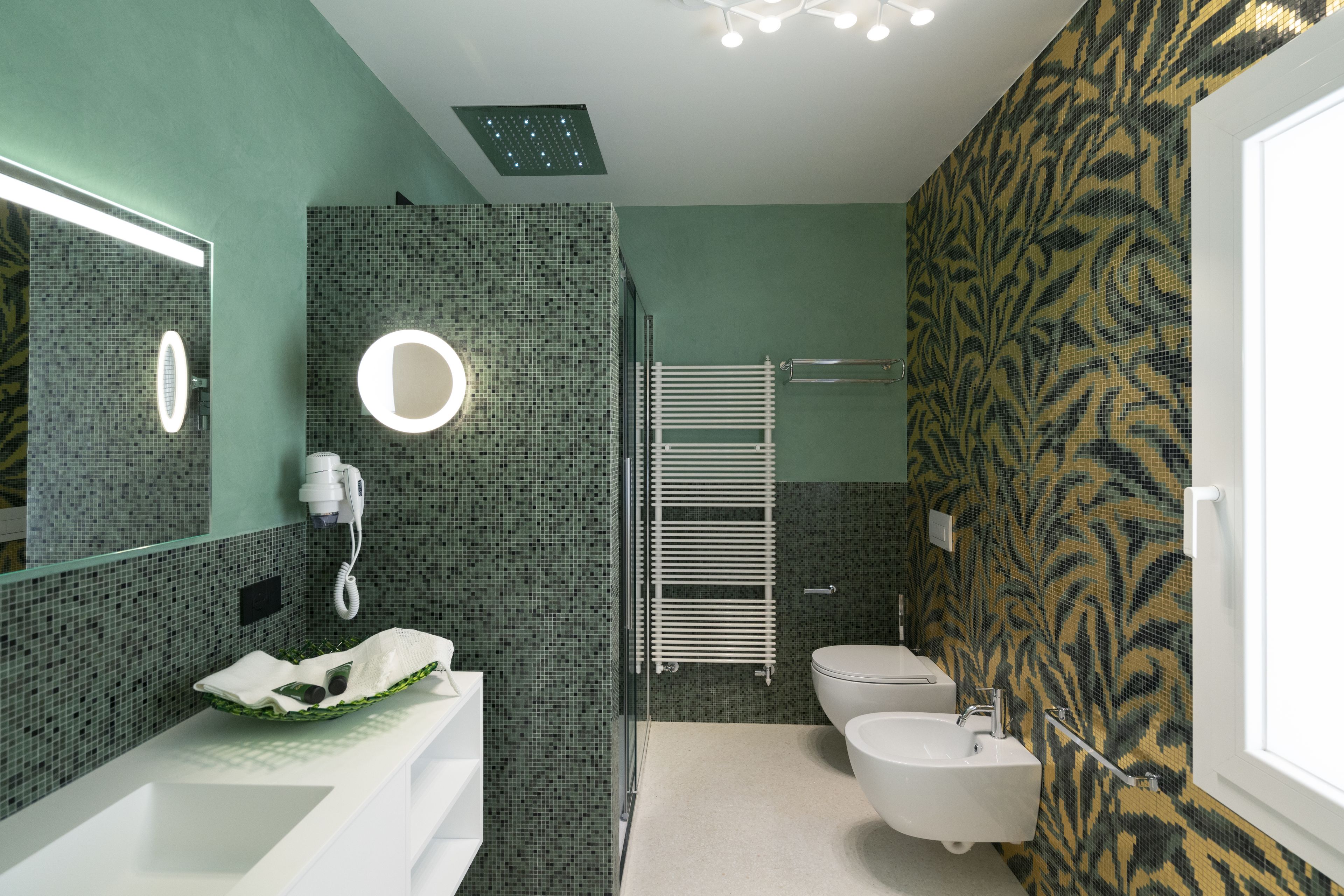 Un baño moderno con un lavamanos blanco, un espejo con luz, un perchero y un inodoro.