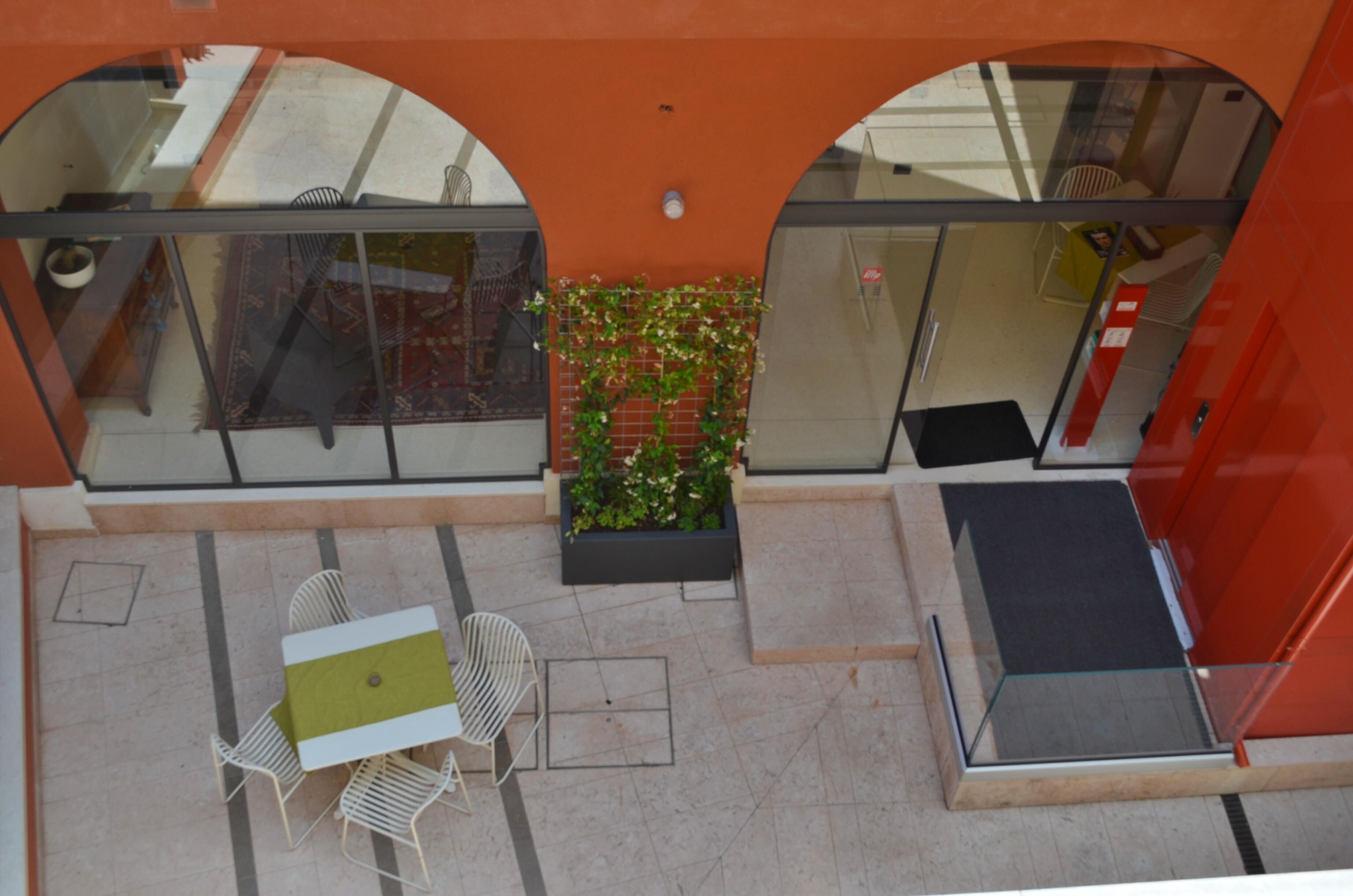 Un espacio al aire libre con mesa y sillas, una jardinera con plantas verdes y una barandilla de vidrio.