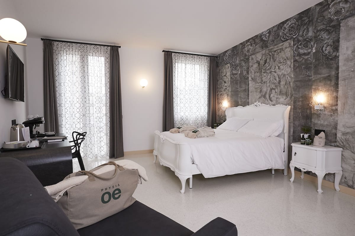 A hotel room with a bed, bedside tables, a desk with a chair, a sofa, and a large bag on the floor.