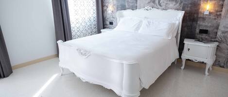 Una cama blanca en una habitación con pared de diseño marmolado y una mesita de noche con lámpara.