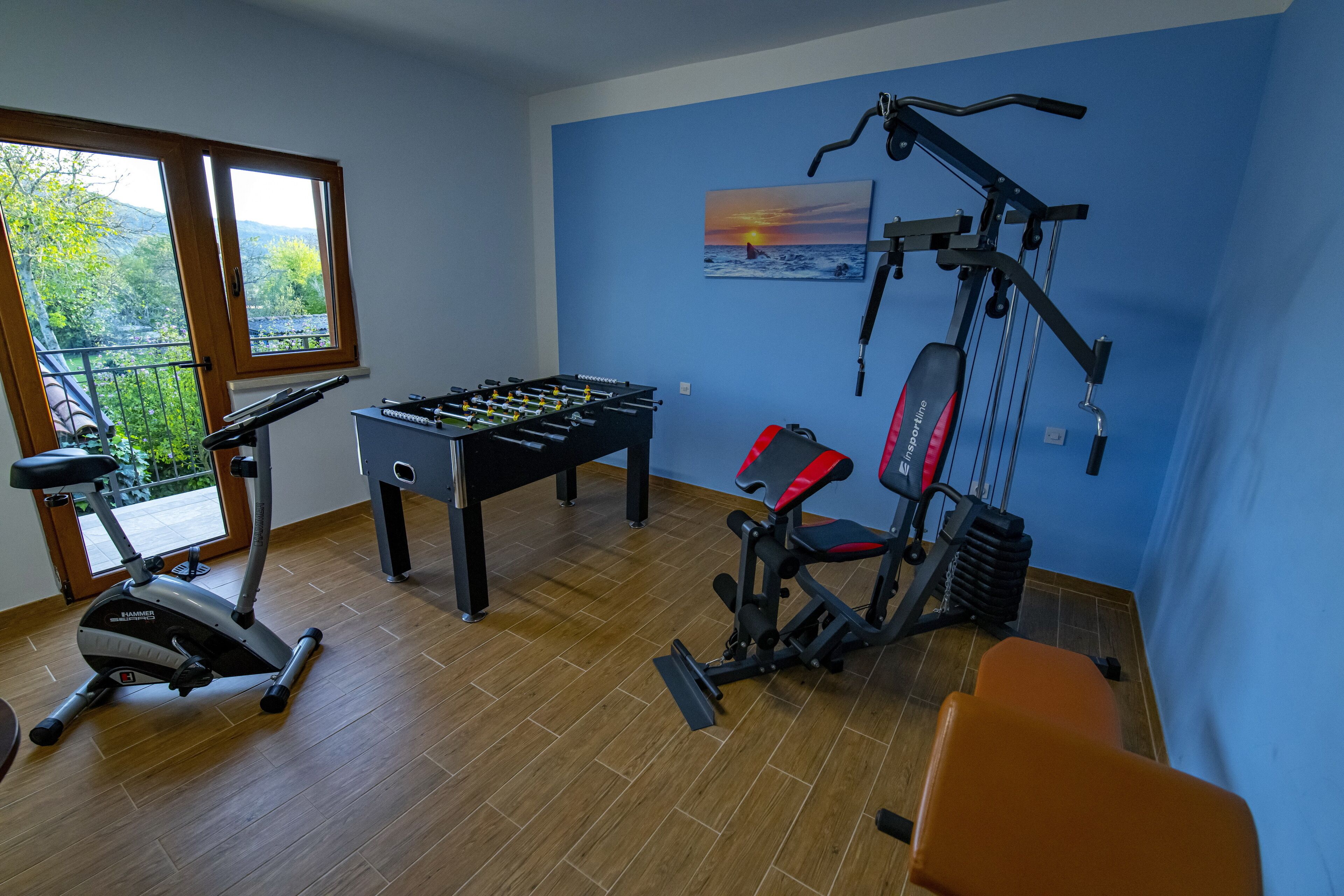 A gym with exercise equipment, a foosball table, and a view of the outdoors.