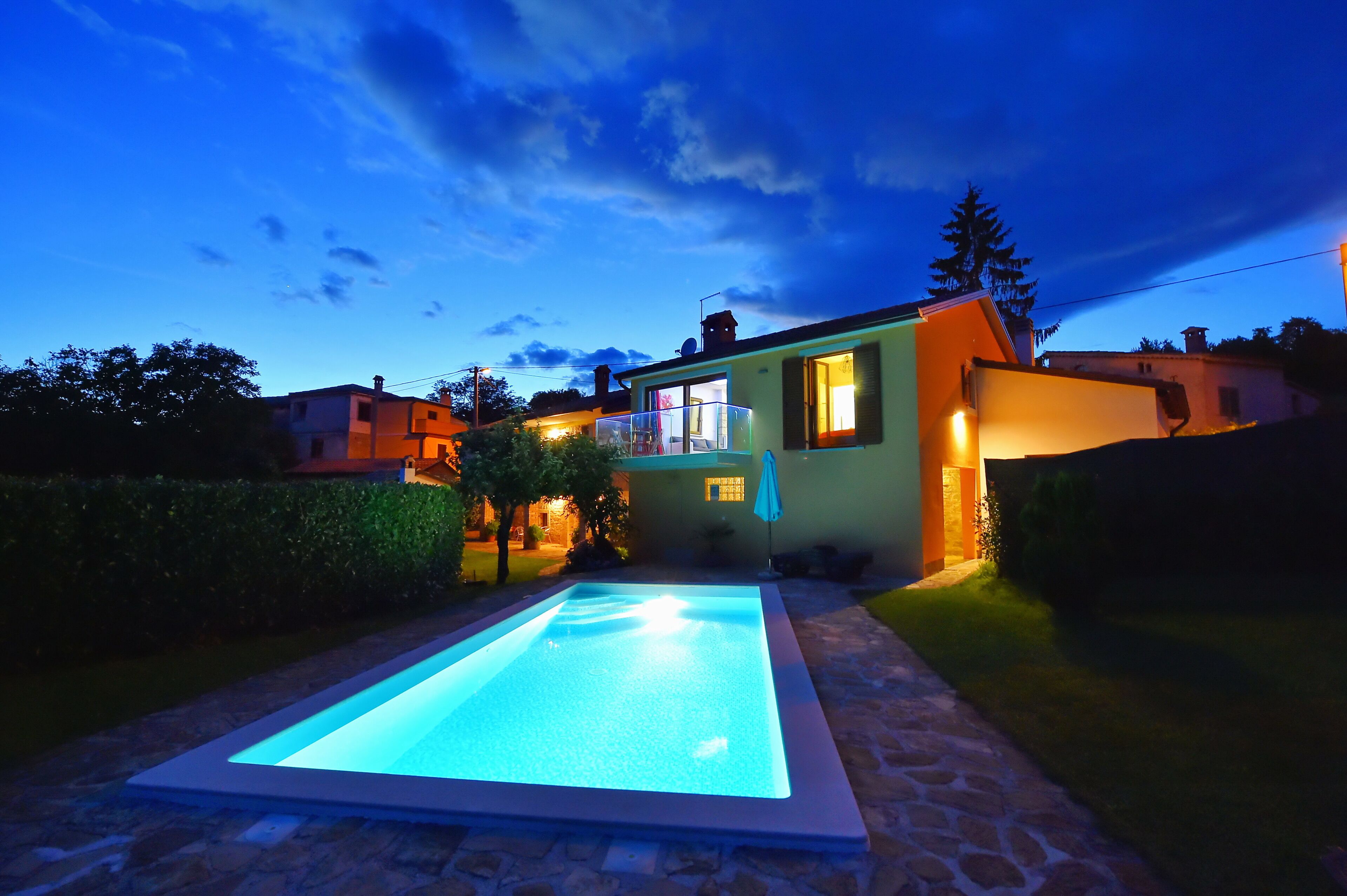 Une maison moderne dotée d’une piscine, entourée d’un chemin en pierre et de verdure.