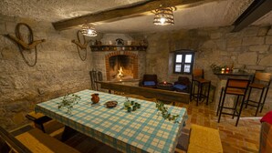 A rustic dining area with a checkered tablecloth, stone walls, a fireplace, and wooden benches.
