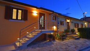 A two-story house with a staircase leading to the upper floor, outdoor lighting, and potted plants.