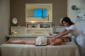 A massage therapy session in a room with a television, shelves with toiletries, and a mirror.