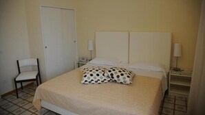 A hotel room with a bed, a chair, a nightstand, and a door. - Via Capo Rooms (Sorrento)