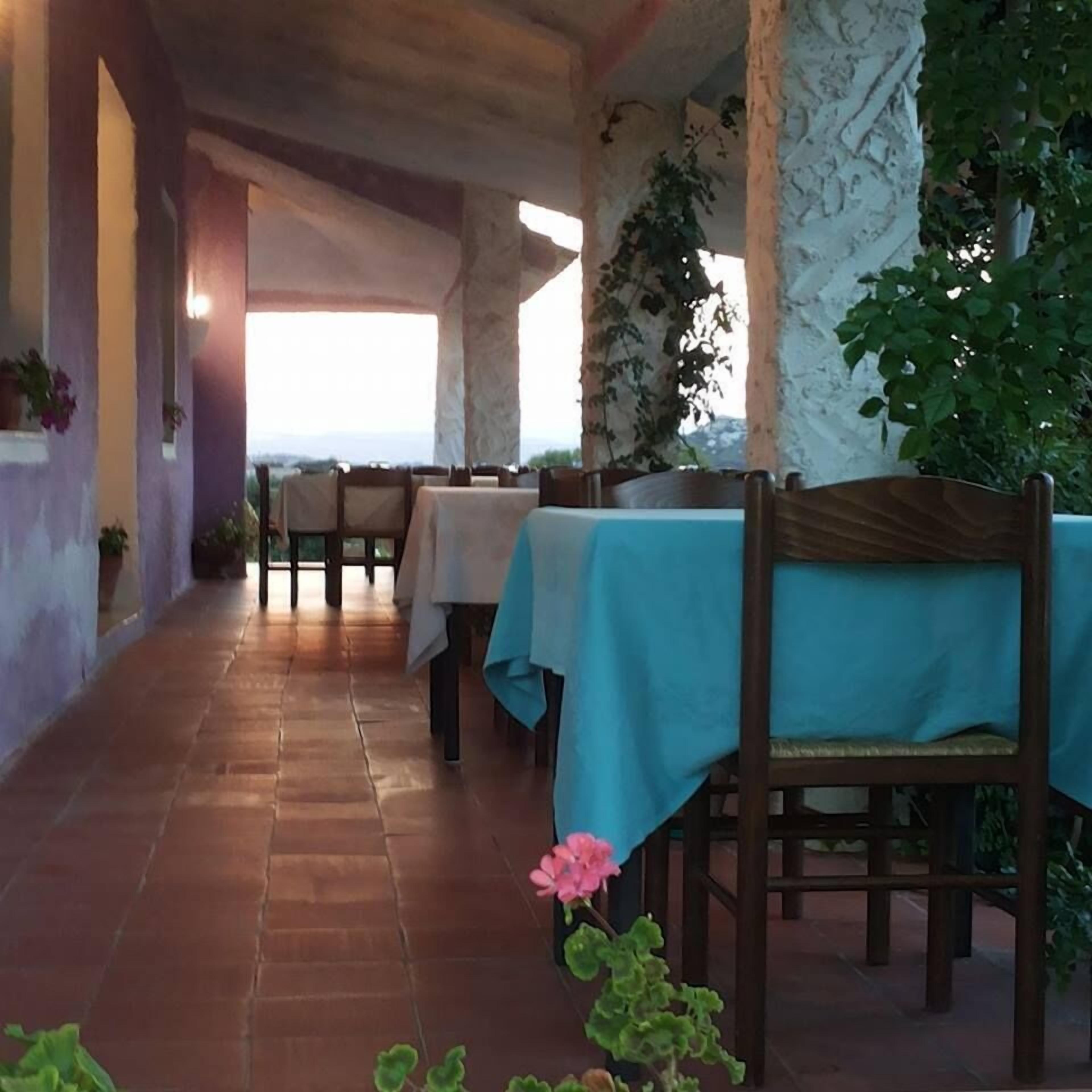 Un espace extérieur aménagé pour les repas, avec des tables recouvertes de nappes bleues, des piliers en pierre et des plantes en pot.