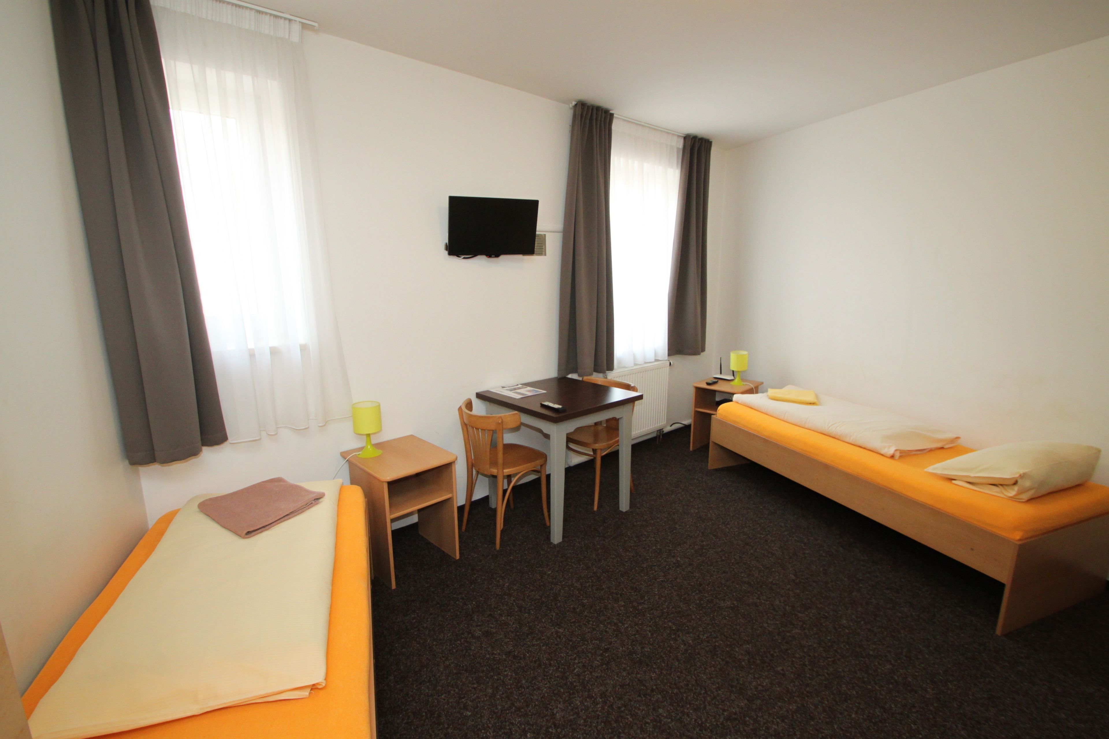 Habitación de hotel con una cama individual, un escritorio con silla, una mesita y un televisor en la pared.