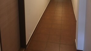 Un pasillo estrecho, bien iluminado, con suelo de baldosas, una puerta con letrero de prohibido fumar y un accesorio de iluminación en el techo.