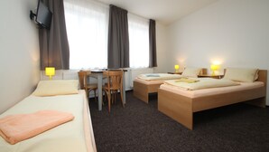 Habitación de hotel con dos camas individuales, un escritorio con silla, un sofá y un televisor instalado en la pared.