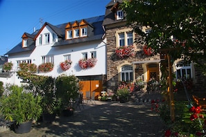A traditional European-style building with a stone facade, multiple windows with flower boxes, and a cobblestone courtyard. - Gästehaus Kiebel (Lösnich)