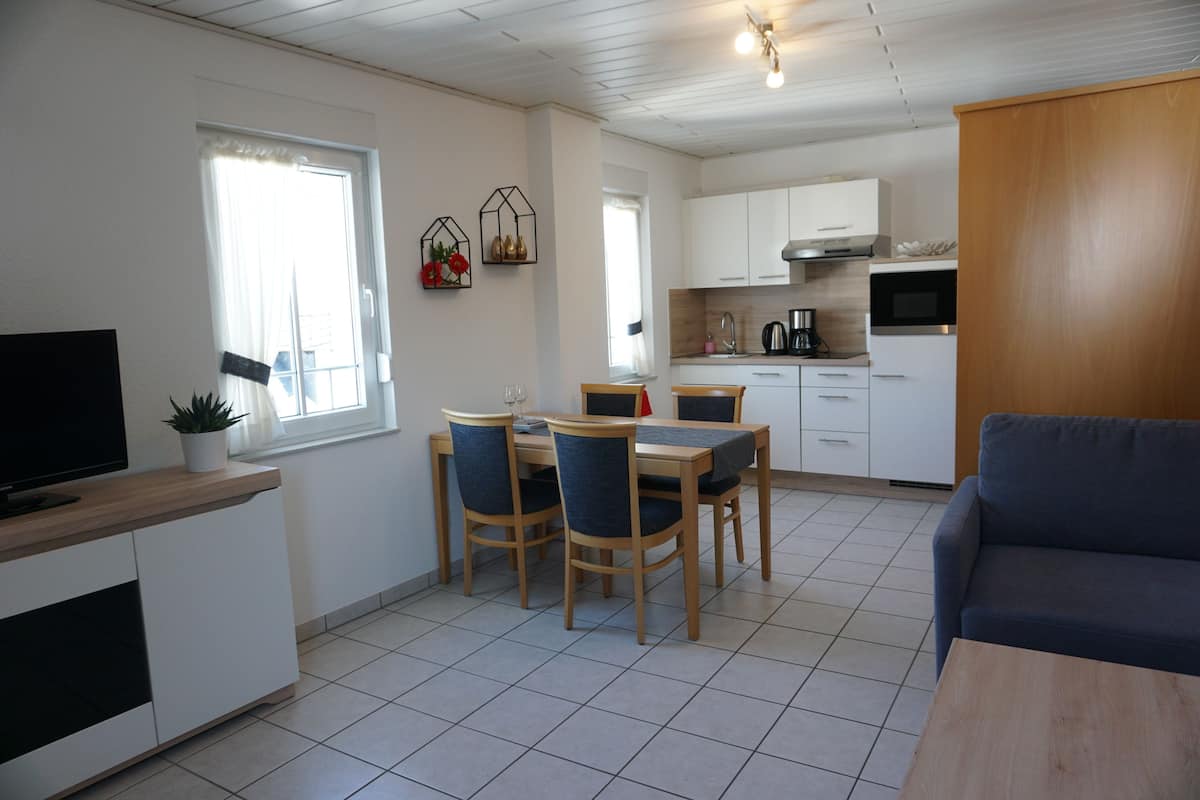Une cuisine moderne avec des meubles blancs, une table à manger avec des chaises, un téléviseur posé sur un meuble en bois et un canapé.