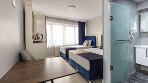 A hotel room with two beds, a dining table, a kitchenette, and a bathroom with a glass shower enclosure. - Sirkeci Family Hotel (Istanbul)