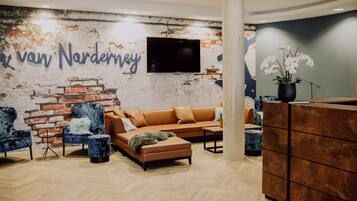 A modern lobby with a brick wall, a sofa, chairs, a TV, and a reception desk.