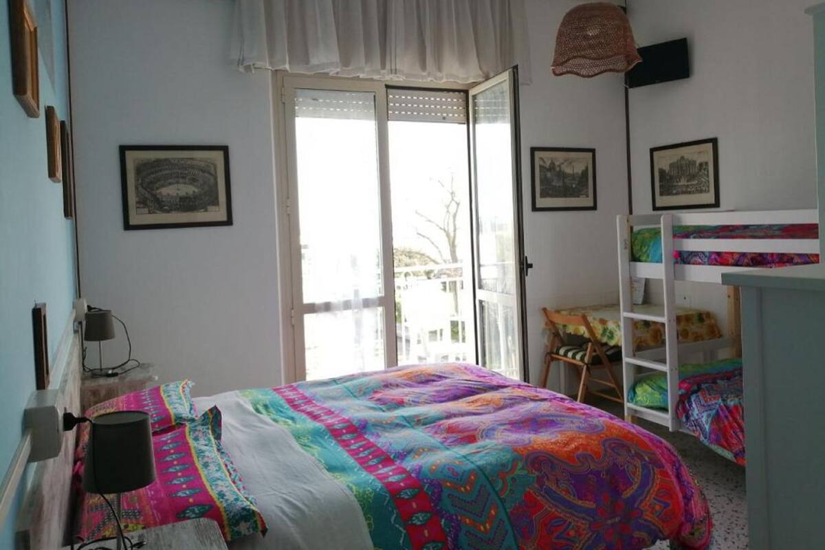 Une chambre à coucher avec une couvre-lit aux couleurs vives, une porte blanche et une fenêtre avec des stores.