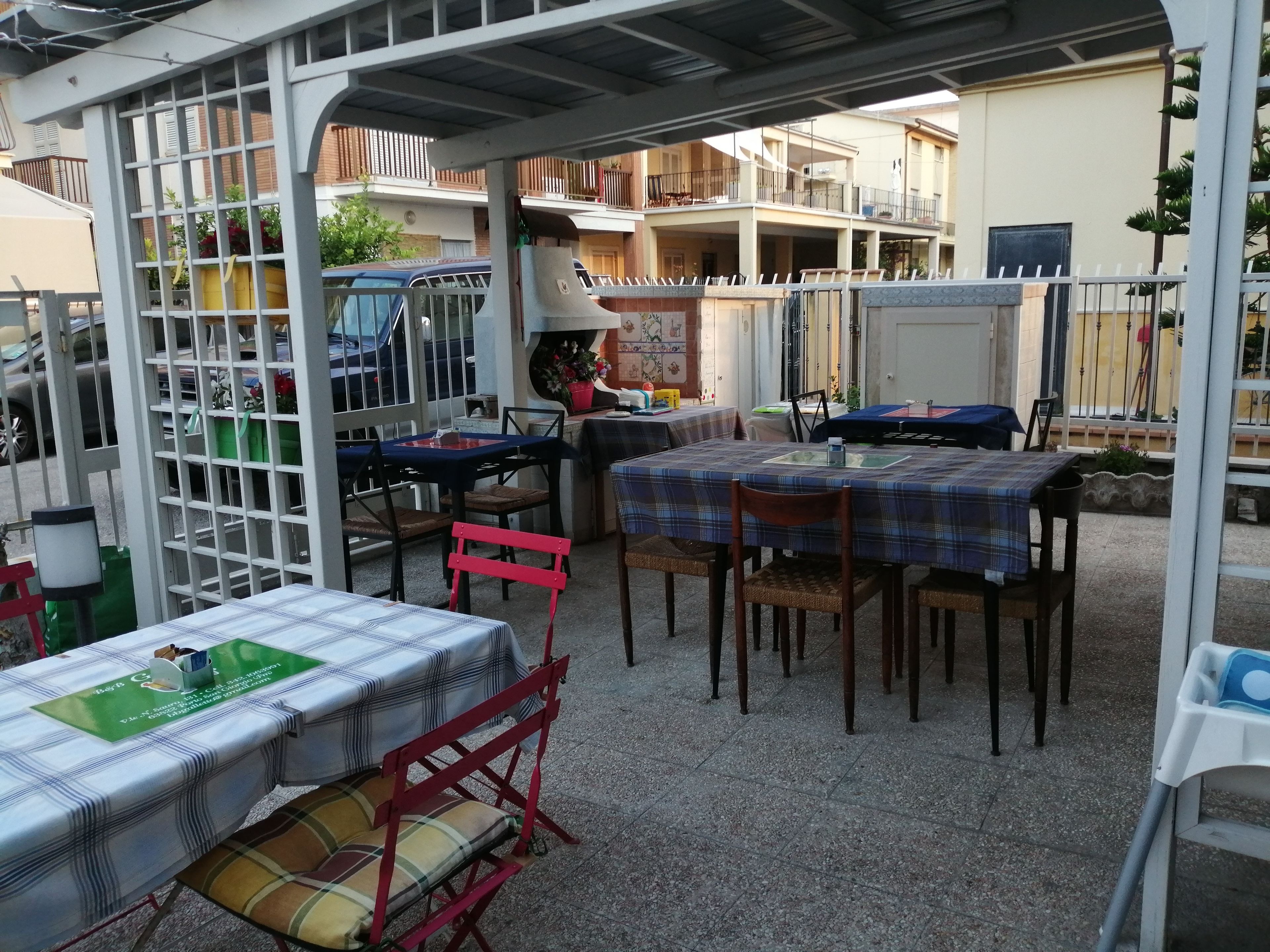 Una zona patio all'aperto con tavoli e sedie, un'area salotto coperta e vista su edifici residenziali sullo sfondo.