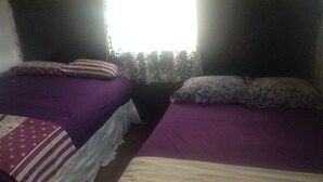 A room with two beds, each with a purple bedspread and white pillows. - Togara Cabin (Victoria Falls)