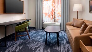 A hotel room with a flat-screen TV mounted on the wall, a desk with a chair, a sofa, a small table, and a lamp. - Fairfield Inn & Suites by Marriott Denver Tech Center North (Denver)