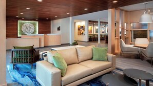 A modern hotel lobby with a reception desk, a beige sofa with green cushions, a small round table, and a blue abstract rug. - Fairfield Inn & Suites by Marriott Denver Tech Center North (Denver)