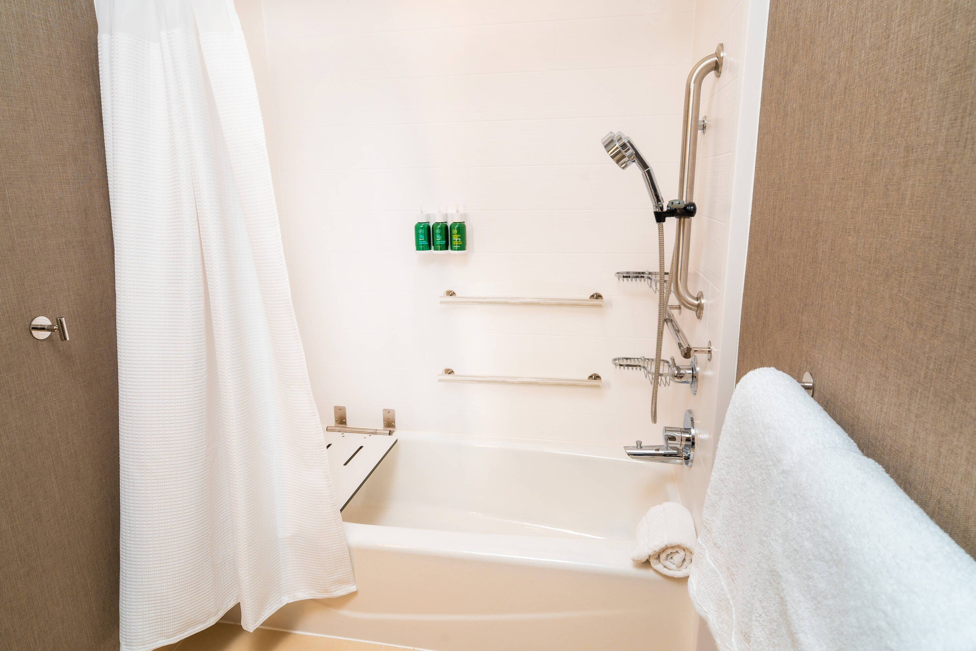 A bathroom with a bathtub, a shower, and a toilet. There are toiletries on the wall and a towel on the floor.