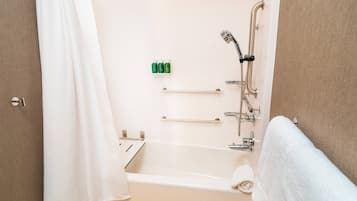 A bathroom with a bathtub, a shower, and a toilet. There are toiletries on the wall and a towel on the floor.