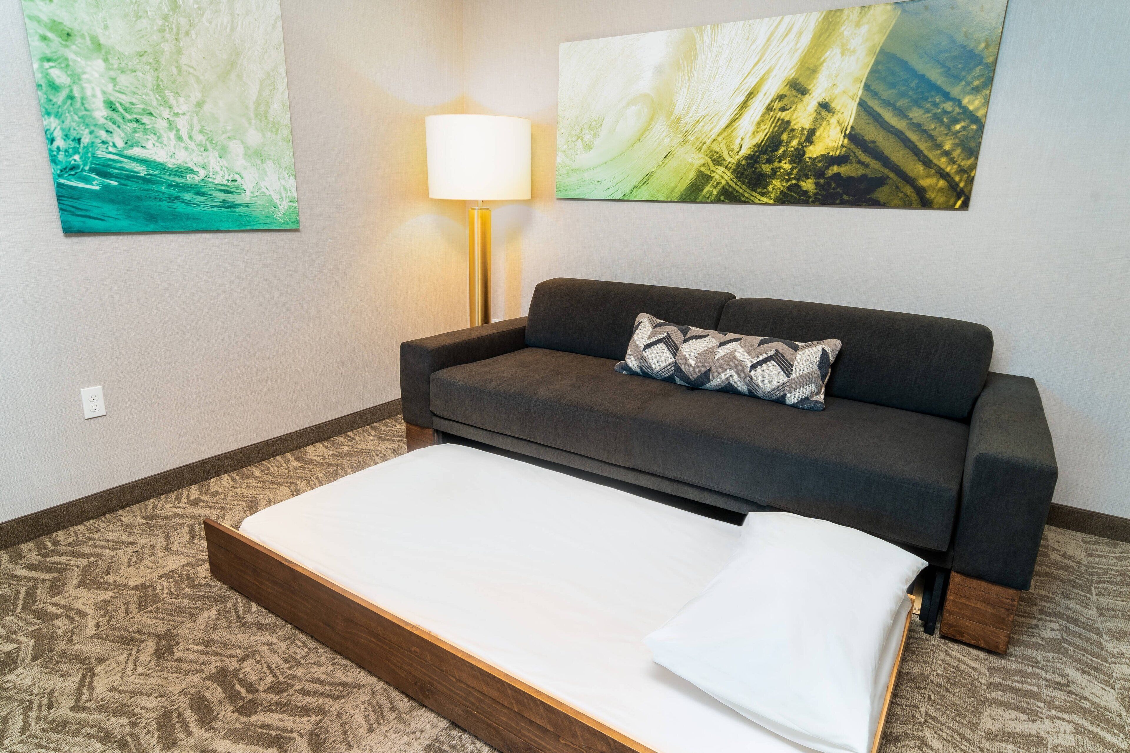 Una habitación de hotel con una cama, un sofá y dos cuadros abstractos en la pared.