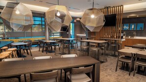 En moderne restaurant med sekskantede hængende lamper, flere siddeområder og et fjernsyn monteret på væggen.