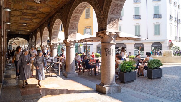 An outdoor café with stone arches, tables, and umbrellas. - Ilsanleonardo - Suites (Bergamo)